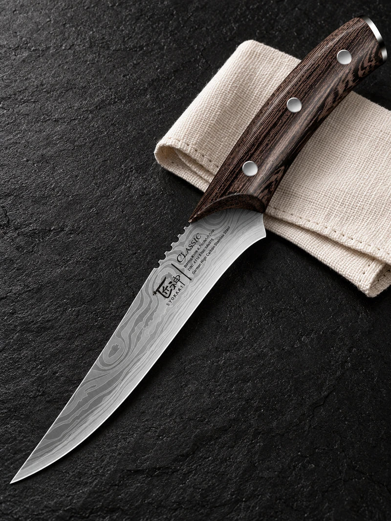One complete curved pointed boning knife on black stone beside a folded cream cloth with its three silver handle rivets and physical blade markings visible