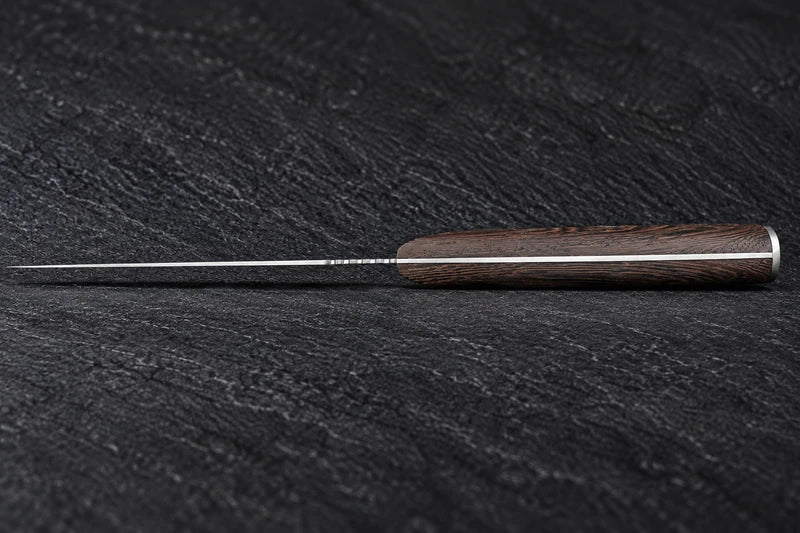 Low edge-on resting view of one boning knife with its handle lying flat on black stone and the thin blade plane horizontal