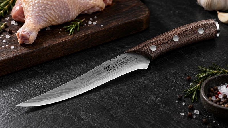 Complete curved pointed boning knife with three silver handle rivets on textured black stone beside poultry on a dark board