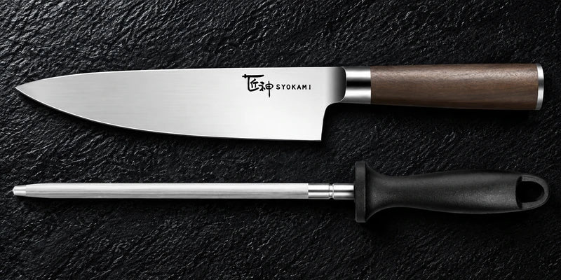 One original plain chef knife and one separate round honing steel with its black loop handle lie parallel on textured black stone